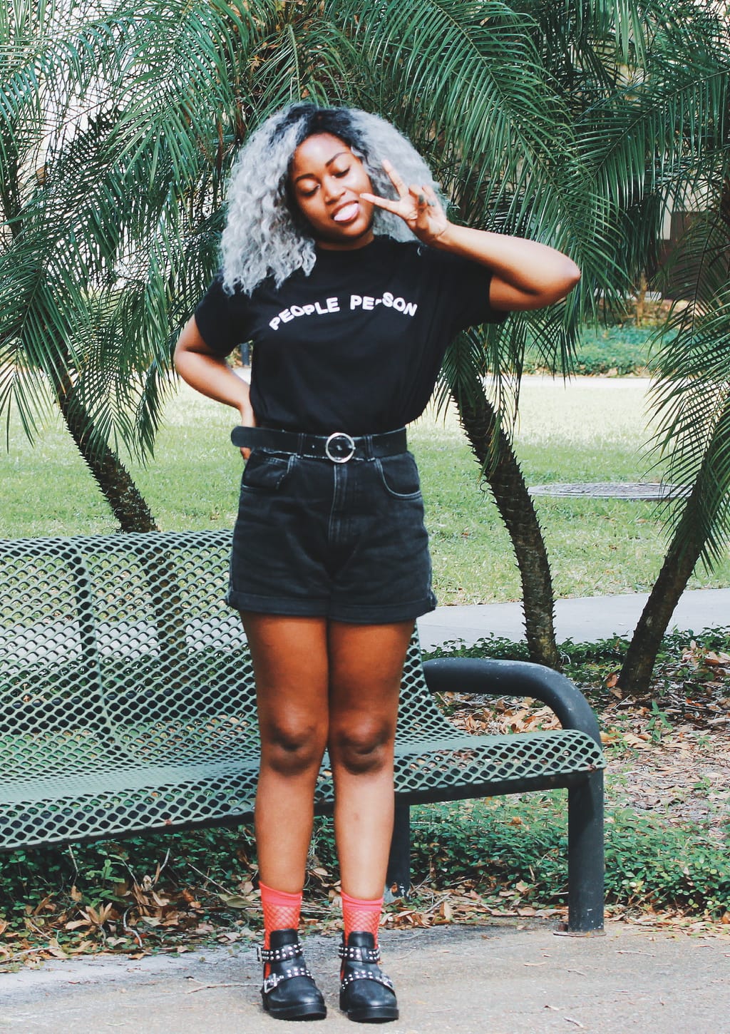 University of South Florida student Lundyn wears an all-black summer grunge look. Her tucked-in t-shirt reads "people person," which she pairs with high-waisted and belted black denim boyfriend shorts and chunky, studded sandals with red fishnet socks.